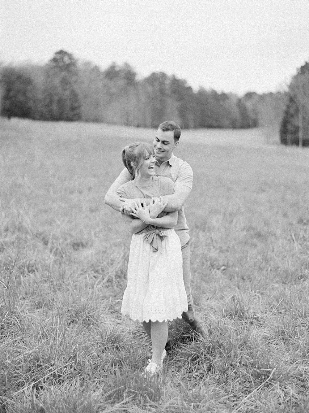 black and white photo of a guy hugging a girl from behind and she's laughing at him.