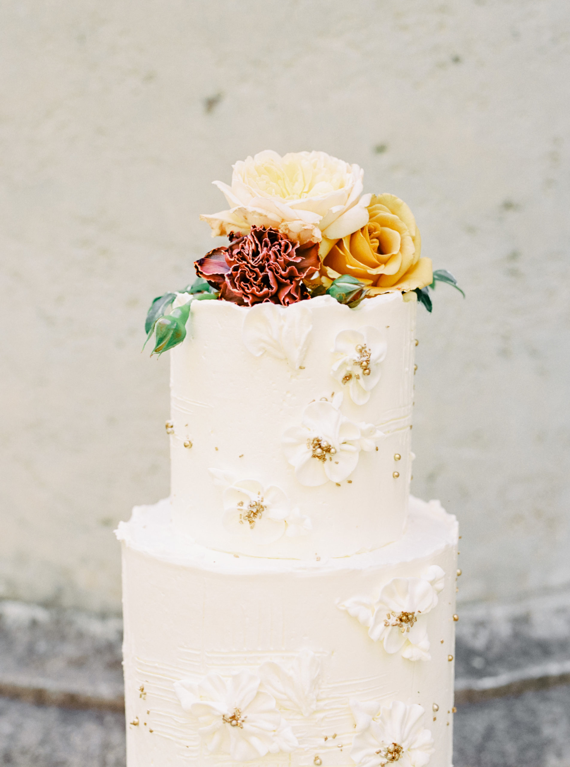 Wedding cake topped with flowers and decorated with white, buttercream flowers and gold accents