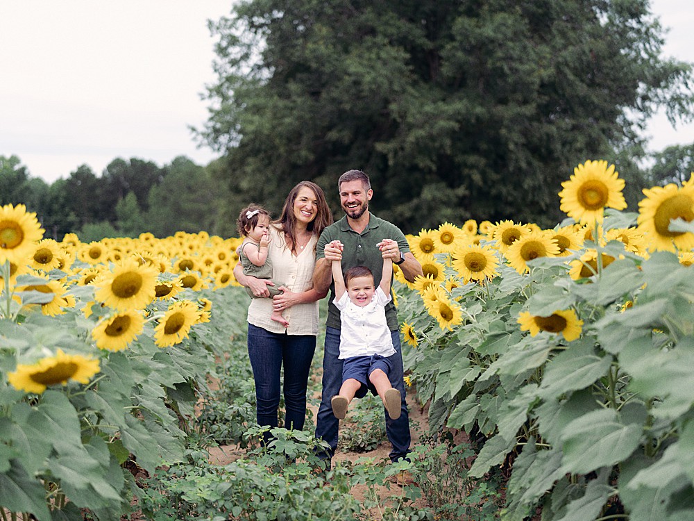 Mom and dad with their two young children in a sunflower field in Georgia