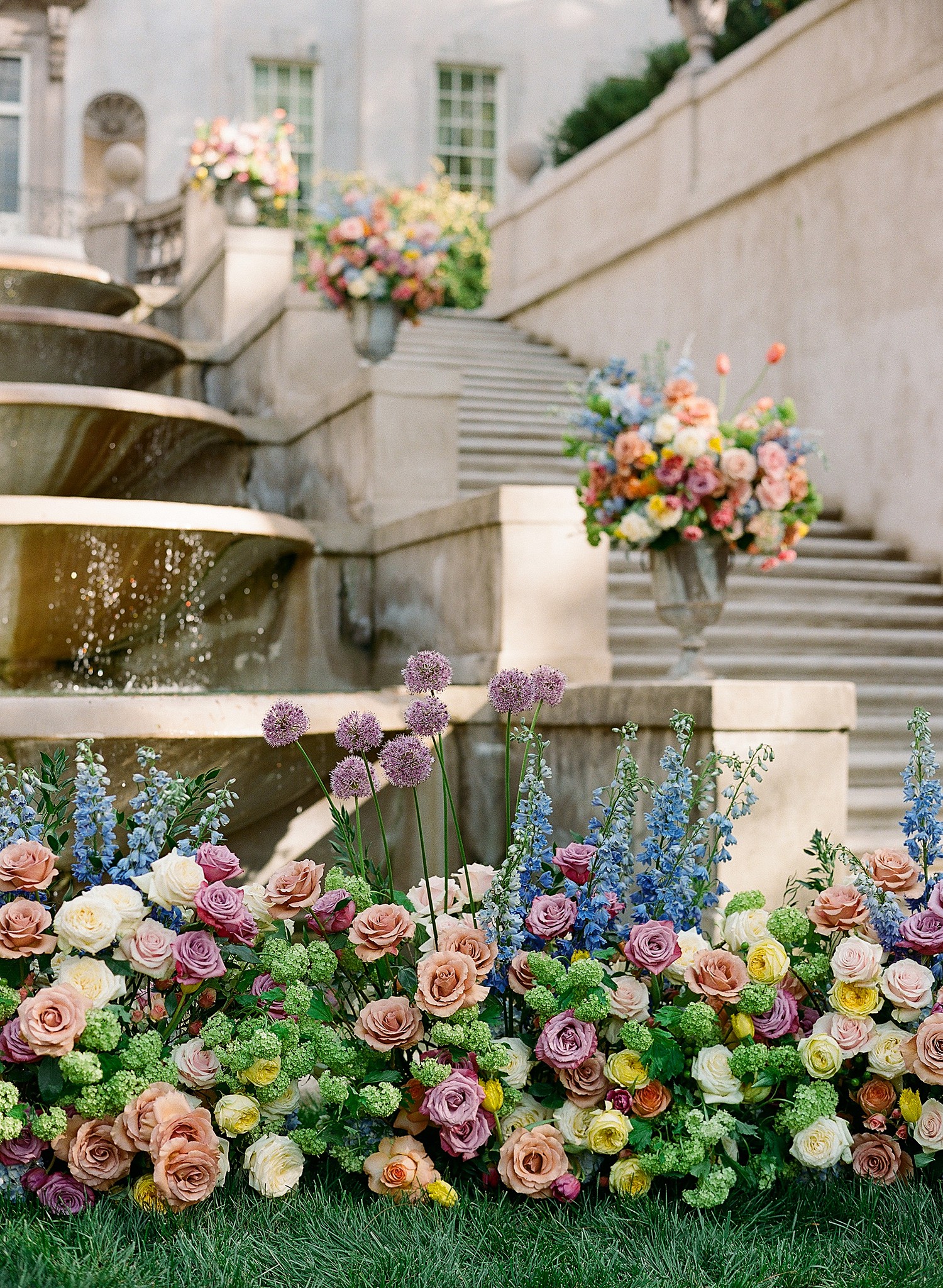 Colorful flowers adorn the ground before the fountain of the Swan House.