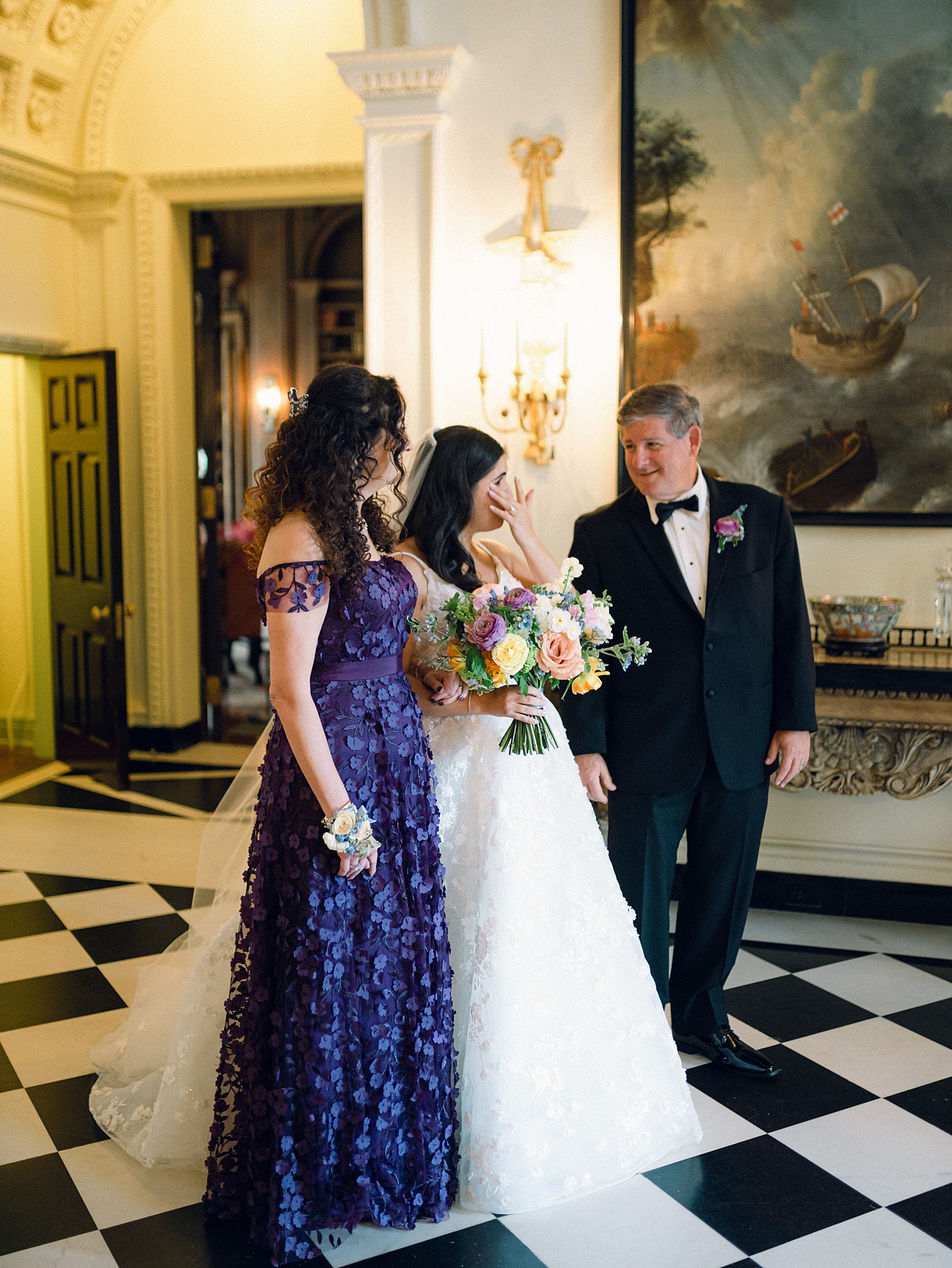 A bride wiping her eyes before walking down the aisle with her parents