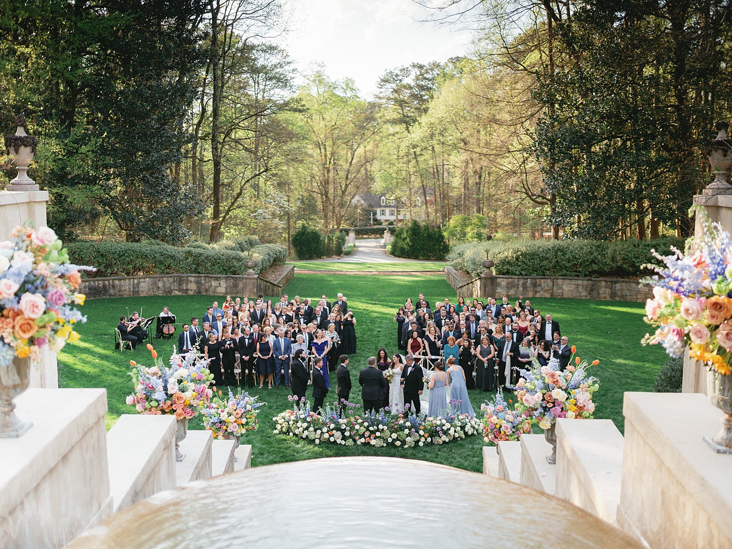 A ceremony taking place on the back lawn of the Swan House before the fountain and staircase.