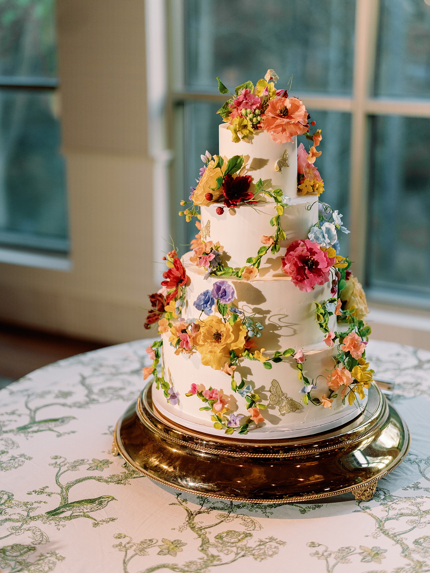 Four tiered wedding cake adorned in flowers and butterflies