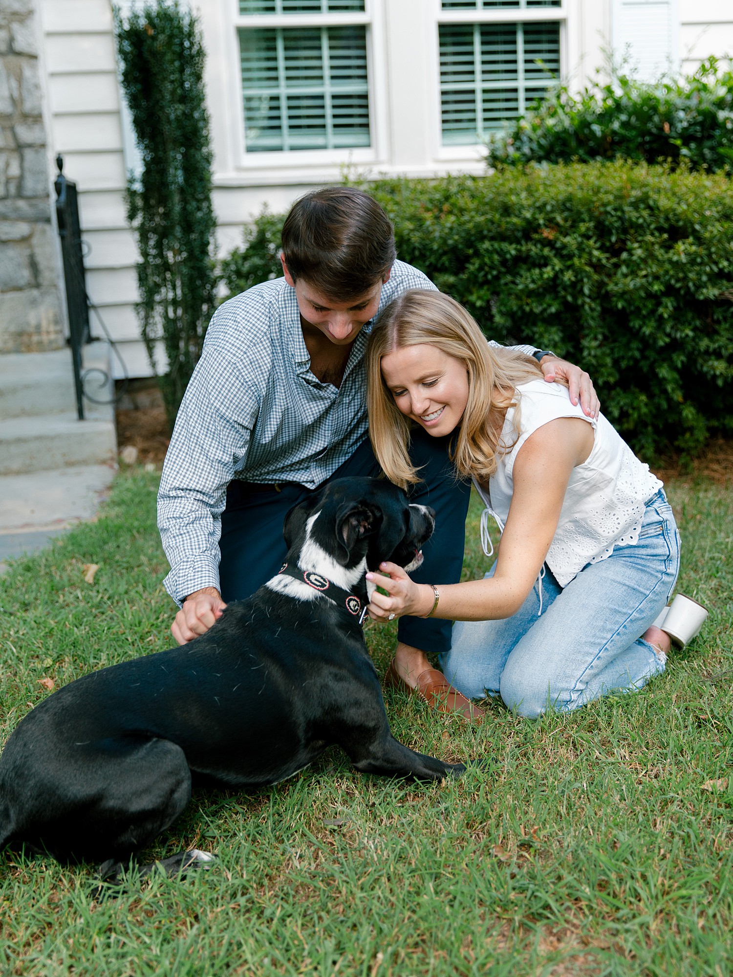 A couple pets their dog in their front yard