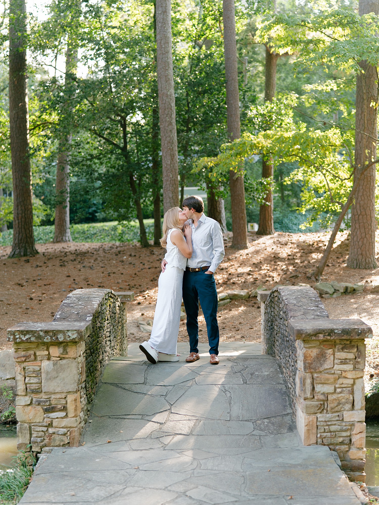 An engaged couple kisses on the stone bridge at Duck Pond in Atlanta