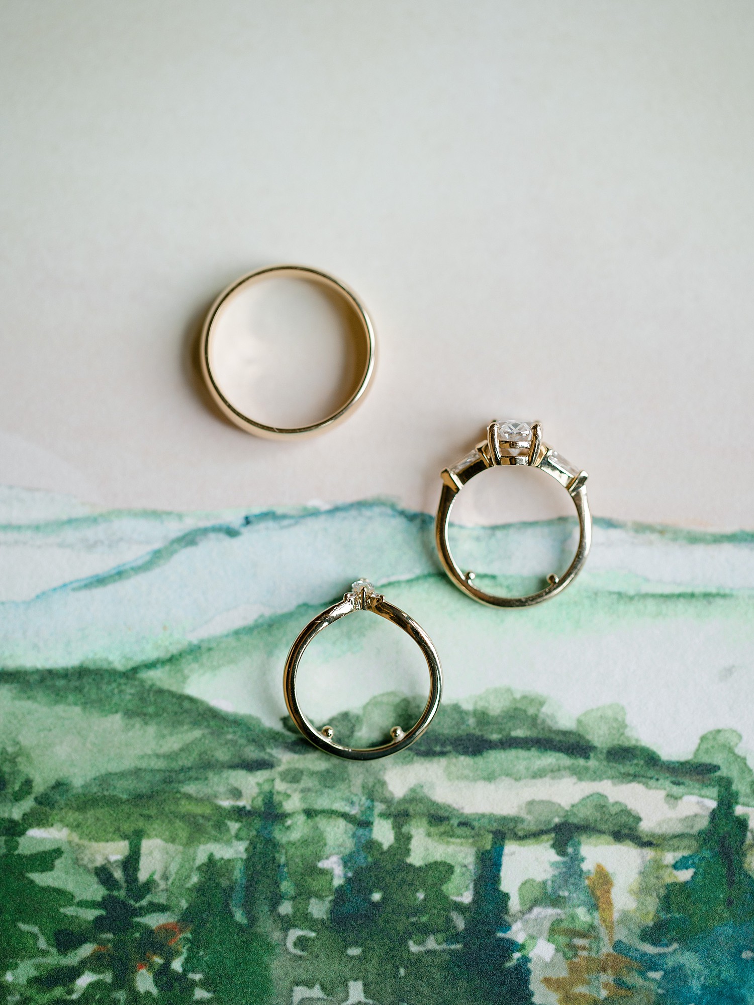 Three rings on a close up of the invitation lining that features a watercolor of the Blue Ridge Mountain range