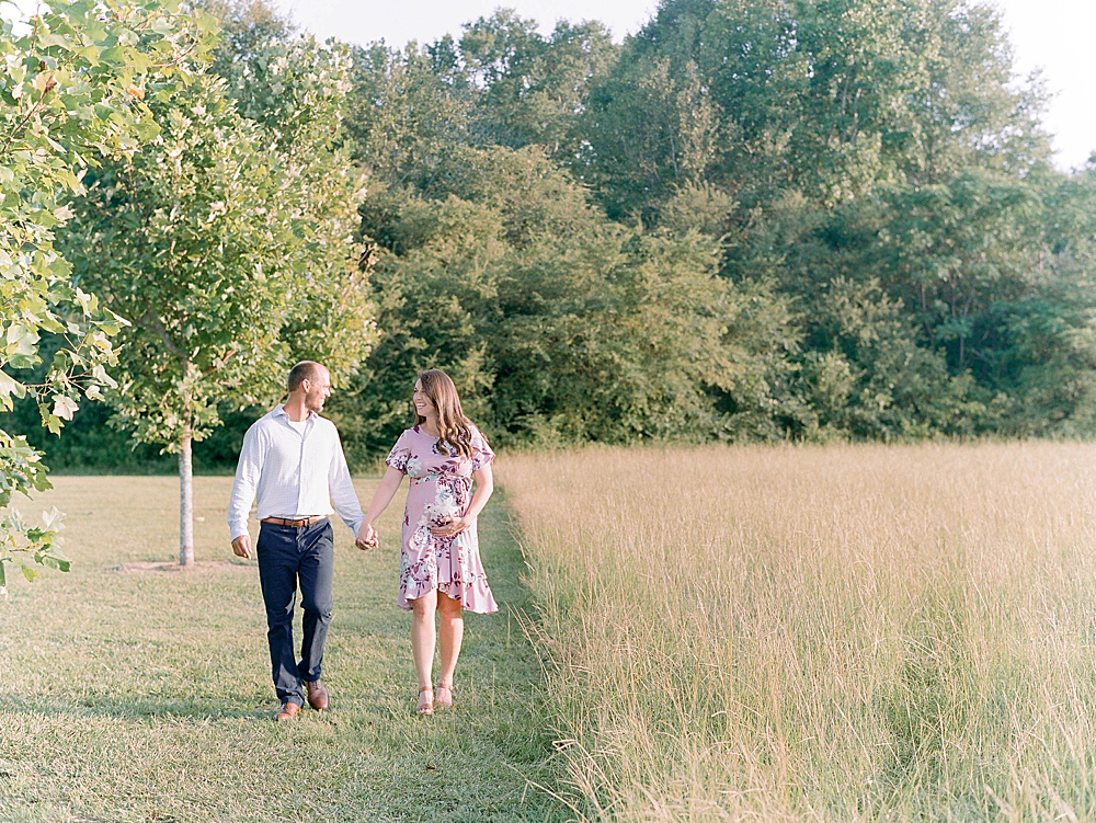 An expecting couple walks through an open field at Kiesel Park in Auburn, Alabama