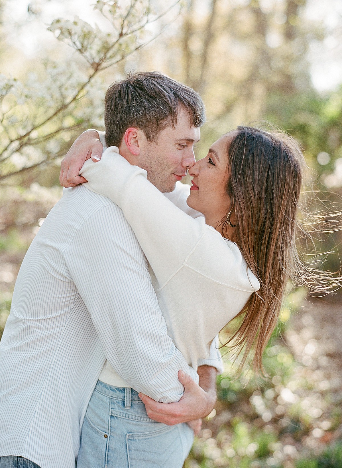 Young couple smiling nose to nose and embracing in a hug amid dogwood blooms at Piedmont Park