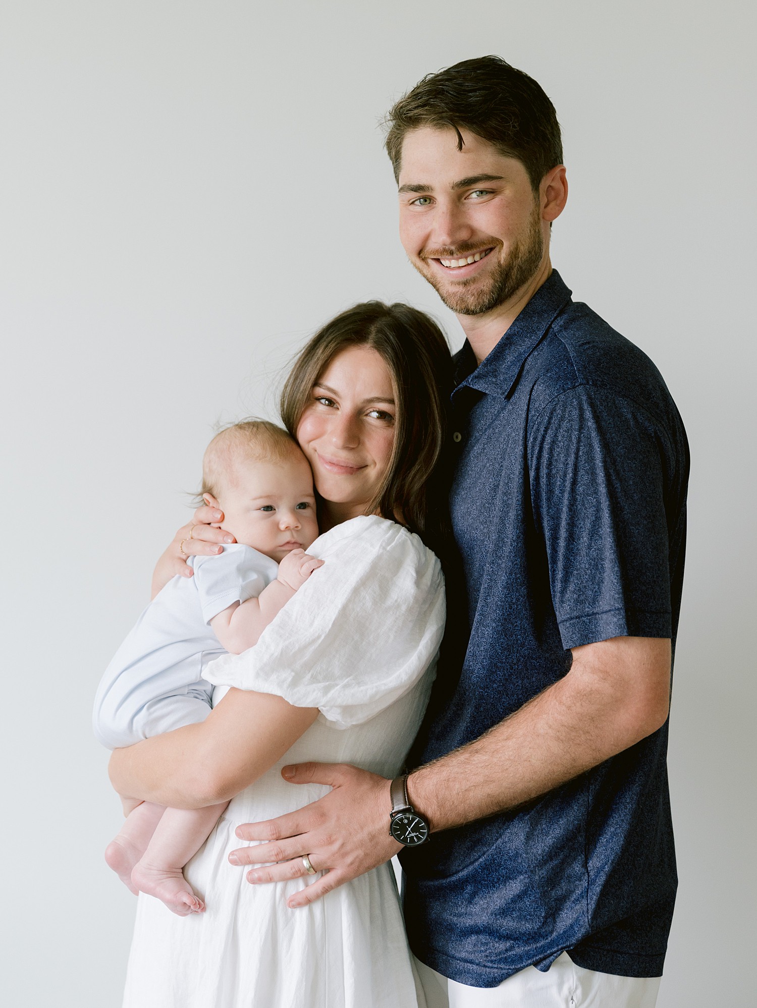 Portrait of a new mom and dad with their newborn son against a white backdrop